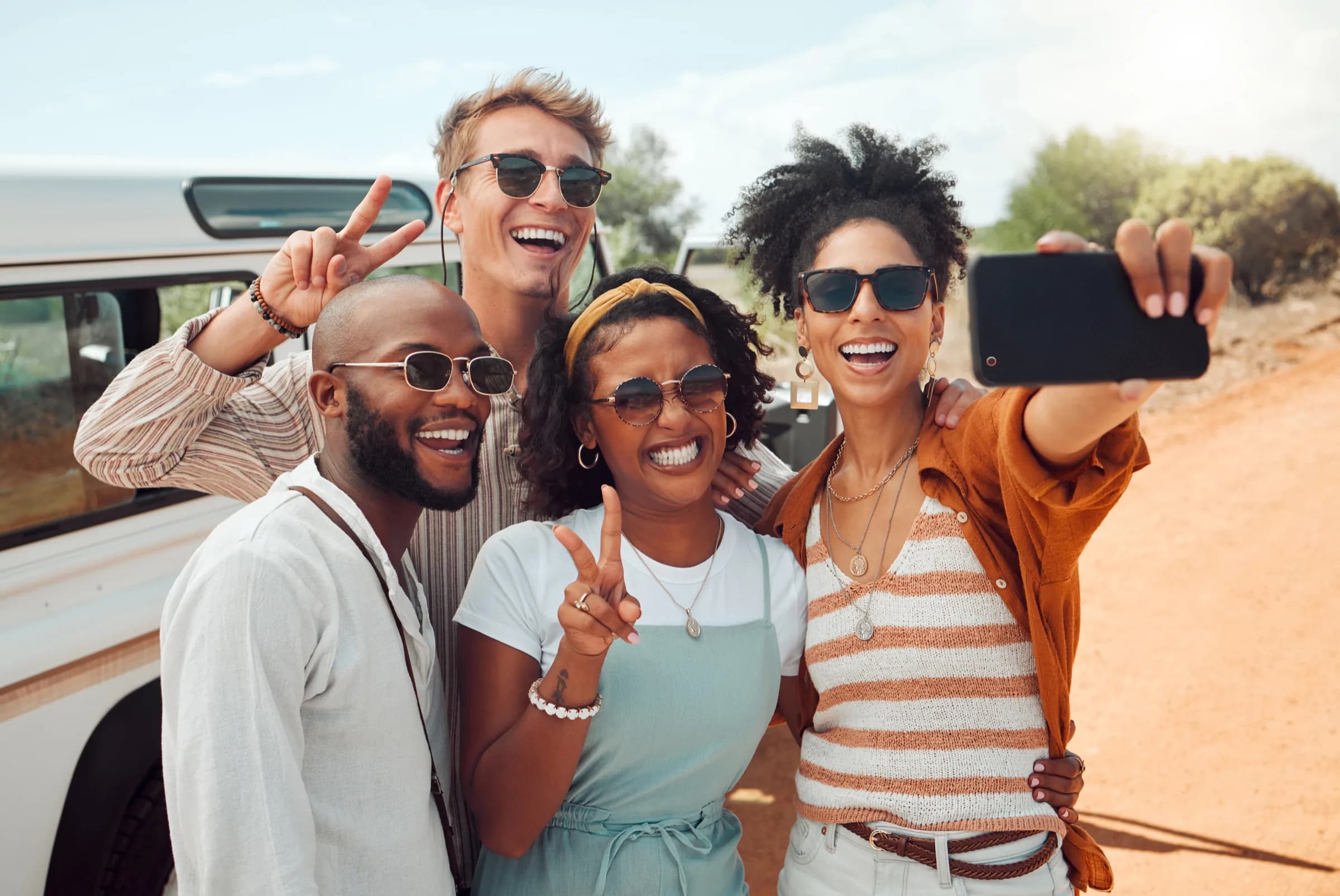 Four friends laughing and taking a selfie together outdoors on a sunny day